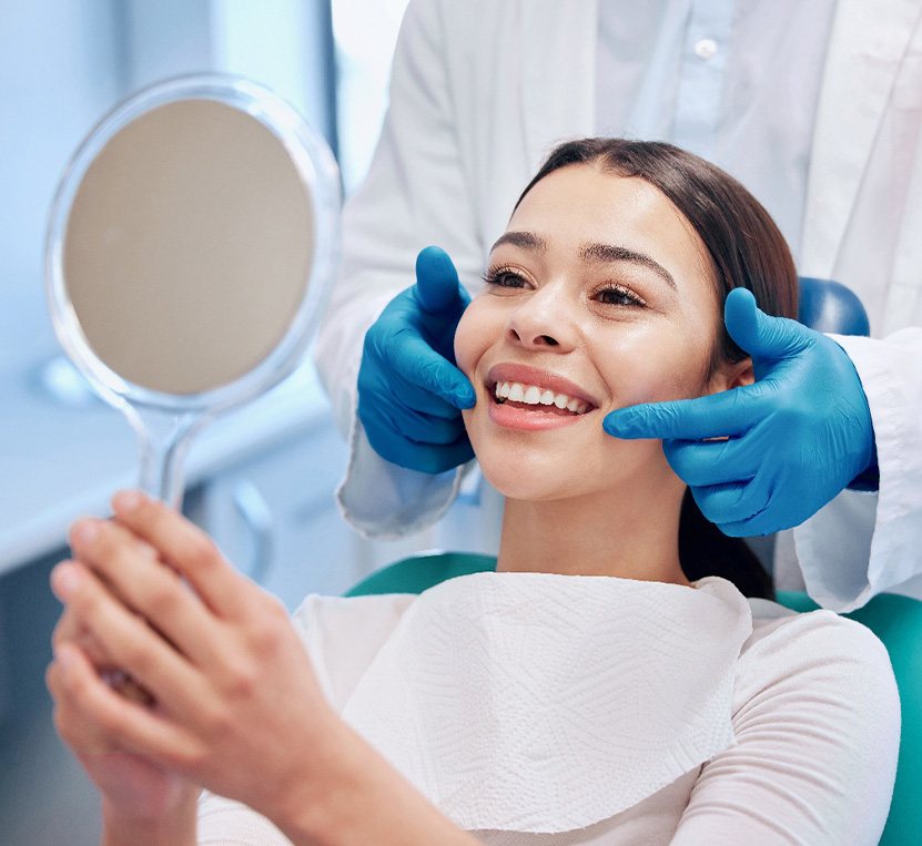 Woman smiling while looking at reflection in handheld mirror