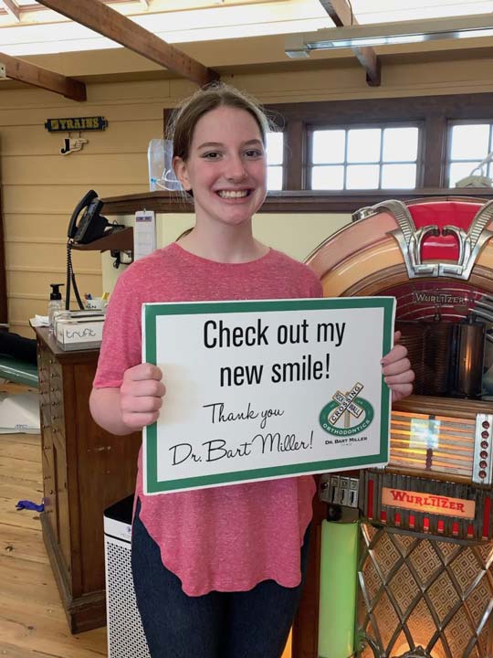 Young female patient in pink smiling with New Smile Sign